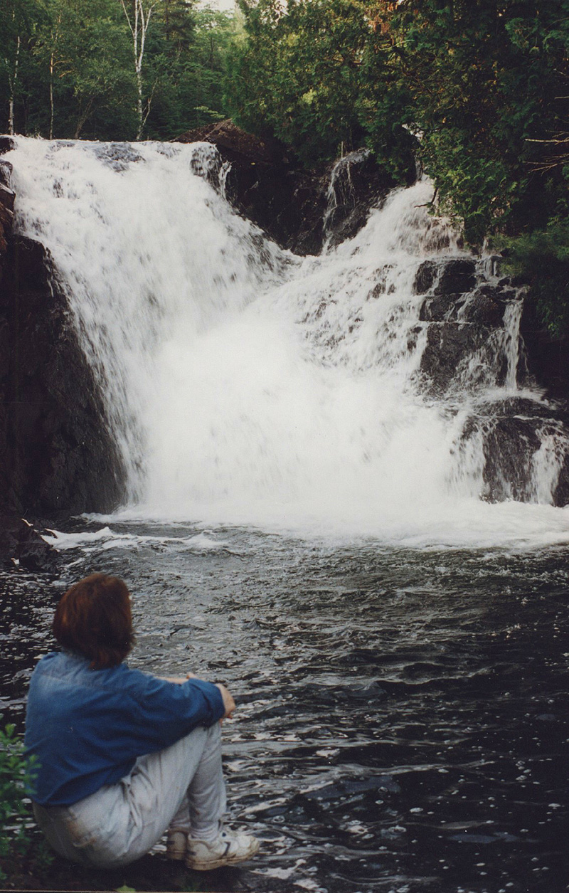 This is a photo of a woman sitting at the bass of a waterfalls